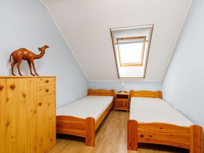 Una habitación pequeña y triangular con dos camas de madera, un aparador de madera y un tragaluz.