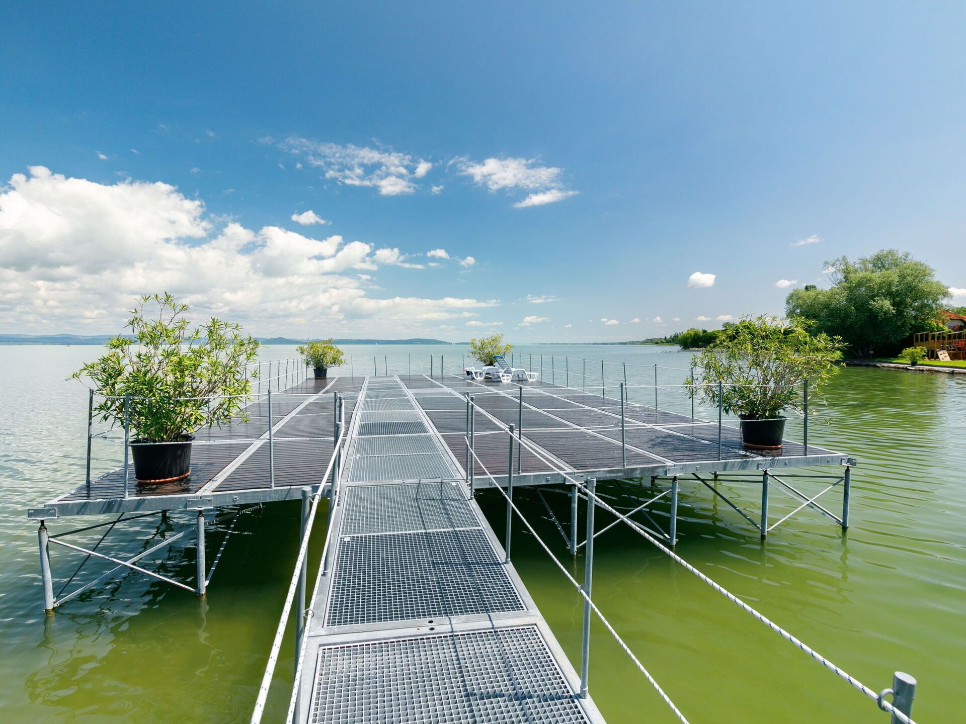 Une jetée qui s’avance dans une étendue d’eau, avec des plantes en pot à chaque extrémité.