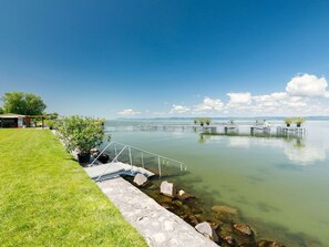 Propiedad frente al lago con un área de césped, un muelle y un edificio pequeño.
