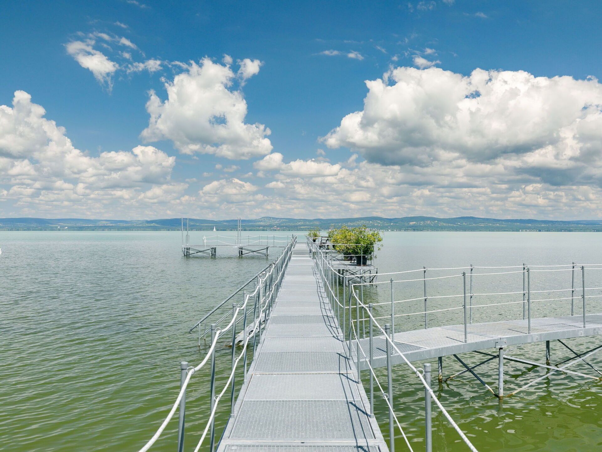 Une longue et étroite jetée s’avance sur un lac paisible, sous un ciel dégagé.
