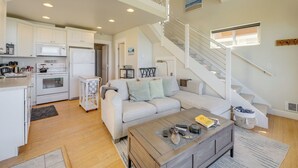 A spacious living area with a staircase, a kitchen with white cabinets, and a cozy seating area. - Cottage at the Beach! Dog Friendly and Free EV Charging with beach access. (Yachats)