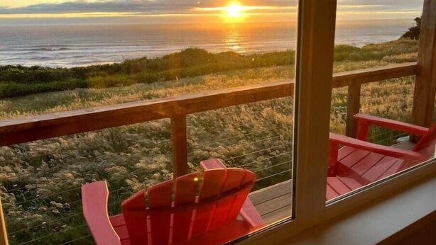 A balcony with a view of the sunset over the ocean, featuring red Adirondack chairs. - Cottage at the Beach! Dog Friendly and Free EV Charging with beach access. (Yachats)