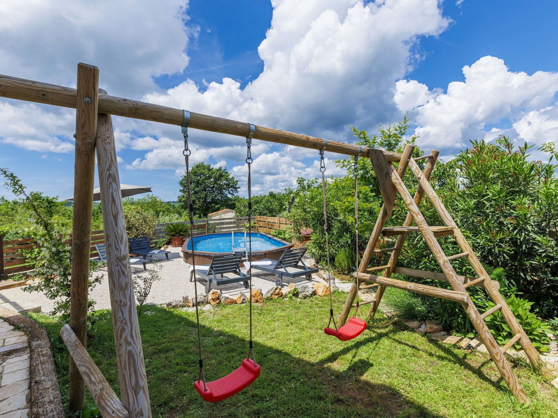 A wooden swing set with two red swings, a wooden ladder, and a pool in the background.