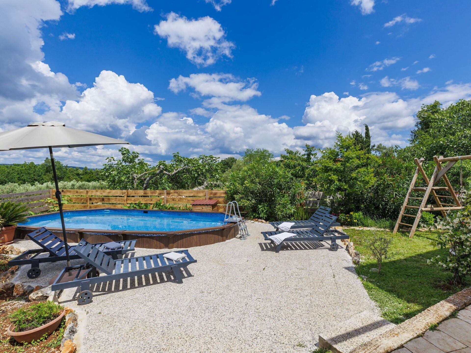 En have med swimmingpool, liggestole og en træterrasse.