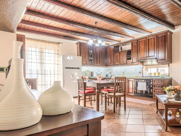 Une cuisine avec des meubles de rangement en bois, un coin repas avec des chaises, un réfrigérateur et un grand vase posé sur le plan de travail.
