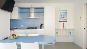 A modern kitchen with a blue countertop, white cabinets, and a stainless steel range hood. There is a dining table with chairs and a bowl of fruit. - Cosy apartment for 6 guests with A/C, WIFI, TV, balcony and pets allowed (Lignano Sabbiadoro)