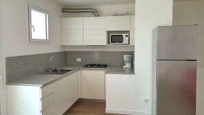 A compact kitchen with white cabinets, a stainless steel refrigerator, a microwave, a gas stove, and a coffee maker. - Cosy apartment for 6 guests with A/C, WIFI, TV, balcony and pets allowed (Lignano Sabbiadoro)