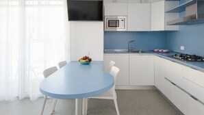 Una cocina moderna con encimera azul, armarios blancos, un microondas, una estufa a gas y un comedor con mesa azul y sillas blancas.