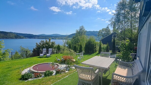 Een verzorgde tuin met een zwembad, tuinmeubels en uitzicht op een meer en bergen.