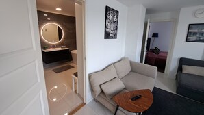 Een moderne woonkamer met een bank, een rond houten bijzettafeltje, een afstandsbediening en een kunstwerk aan de muur.