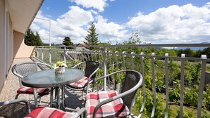 Un balcon avec une table ronde et des chaises en osier, un pot de fleurs et une vue sur un vignoble et des montagnes.