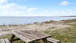 A wooden picnic table on a sandy beach with a view of the sea and a distant shoreline. - 2 bedroom nice apartment in Sydals (Sydals)