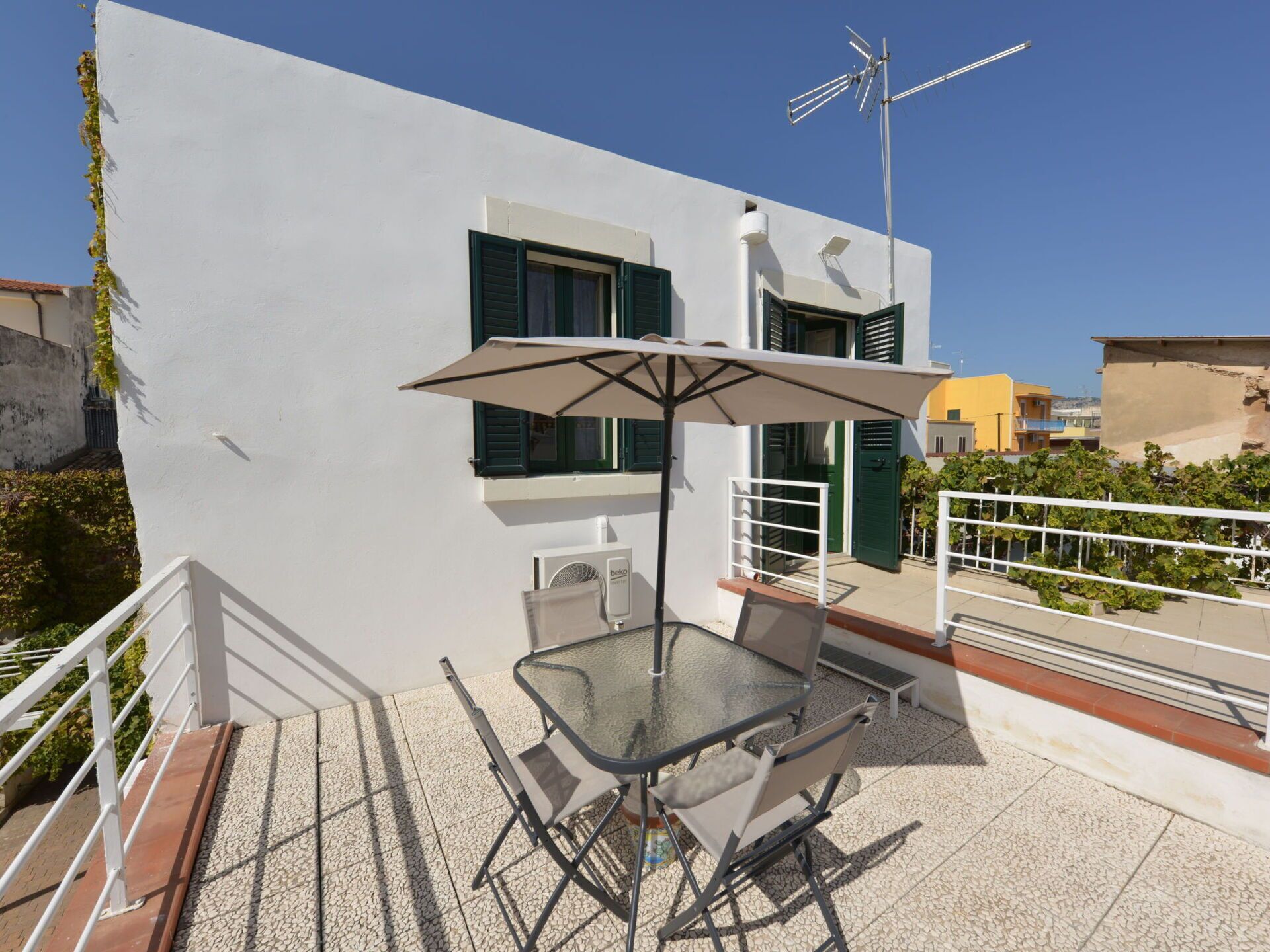 Un balcon avec une table et des chaises en verre, un parasol et une antenne de télévision.