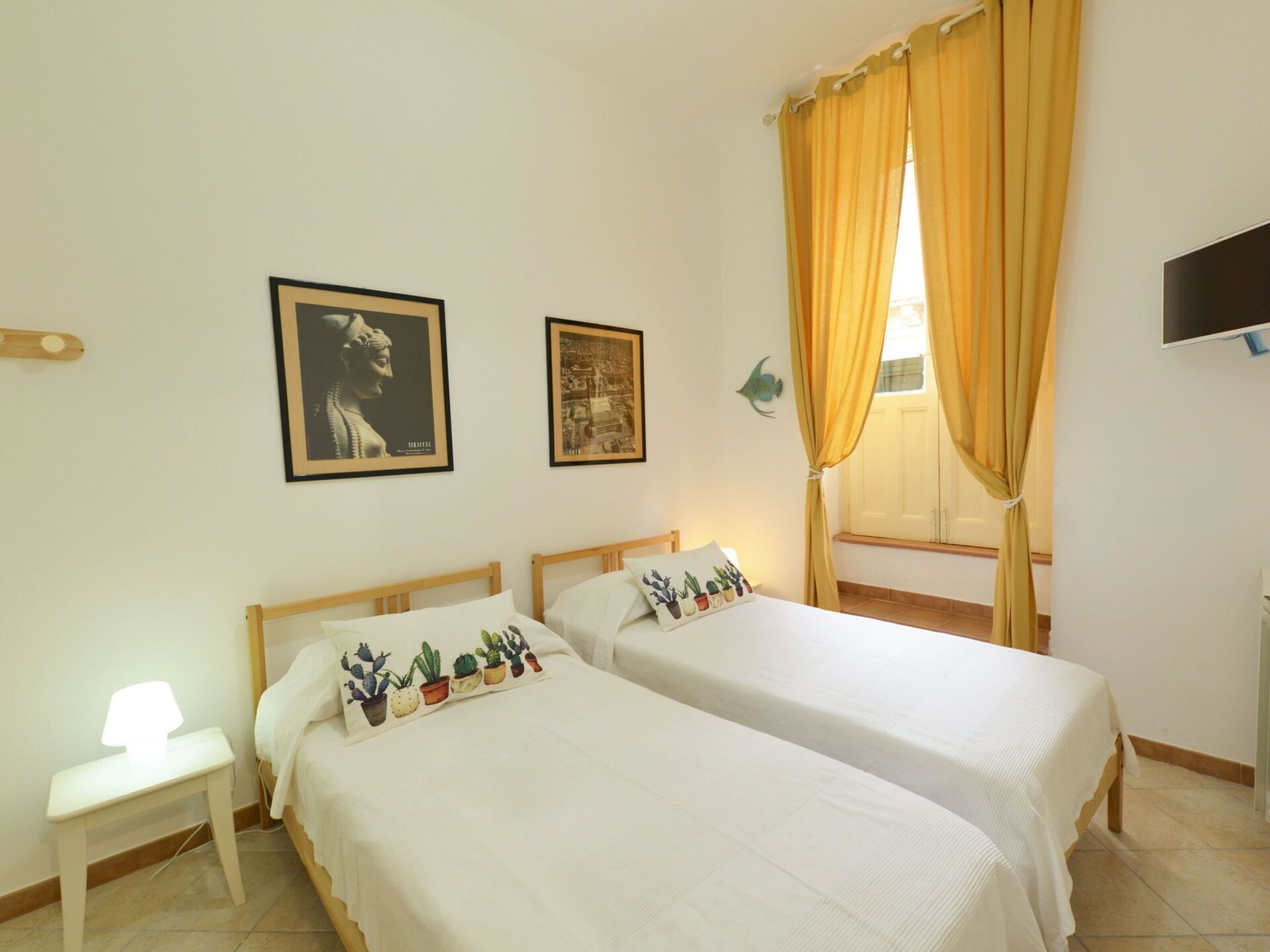 A room with two beds, a small table, a TV, and two framed pictures on the wall.