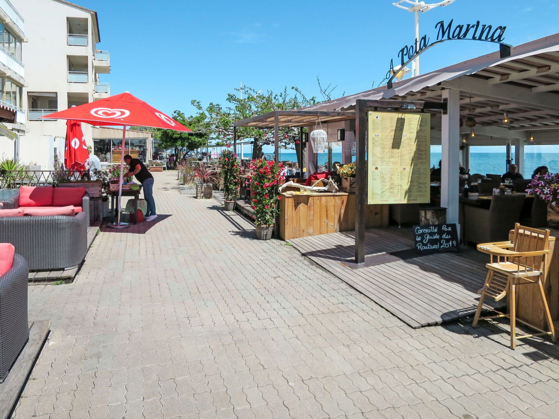 A waterfront restaurant with outdoor seating, a red umbrella, and a sign reading "A Poeta Marina".