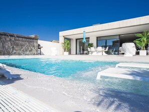Un espace piscine extérieur moderne, avec une piscine à l’eau d’un bleu limpide, des chaises longues blanches et un design architectural minimaliste.