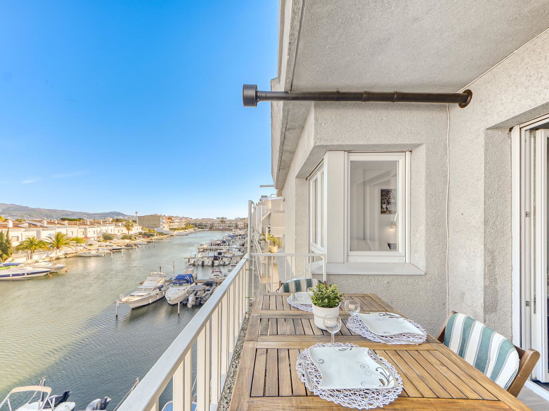 Ein Balkon mit einem Holztisch, gedeckt für ein Essen, mit Blick auf eine Marina und Boote.