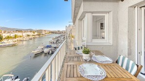 A balcony with a wooden table set for dining, overlooking a marina with boats. - Beautiful apartment for 4 people with A/C, WIFI, TV, terrace and pets allowed (Empuriabrava)