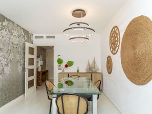 A dining area with a glass table and wicker chairs, a modern pendant light, and decorative wall art.