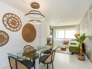 A modern dining area with a glass table, woven wall decor, and a green sofa.