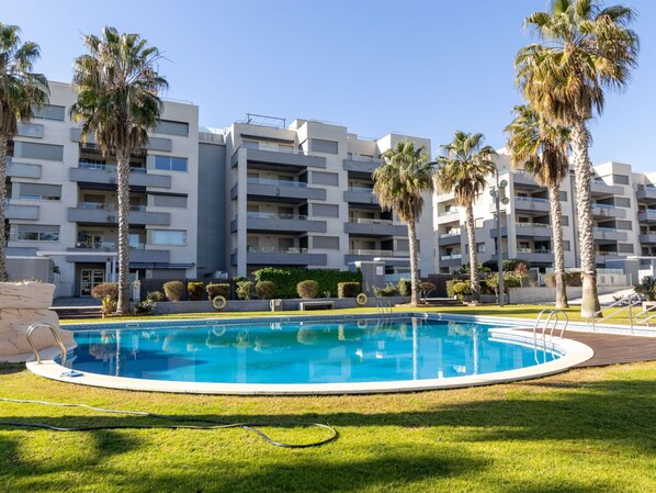 A modern apartment building with a swimming pool surrounded by palm trees and well-maintained grass. - Nice apartment for 4 guests with WIFI, A/C, pool, TV, terrace and pets allowed (Torredembarra)