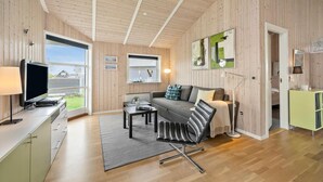 En moderne stue med sofa, sofabord og fjernsyn. Væggene er træ, og der er et stort vindue.