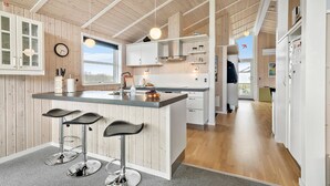 Et moderne køkken med en central ø, barstole, trævægge og et stort vindue.