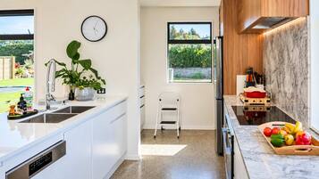 Una cocina moderna con armarios blancos, un lavamanos de acero inoxidable, un reloj en la pared y una ventana con vista al jardín.