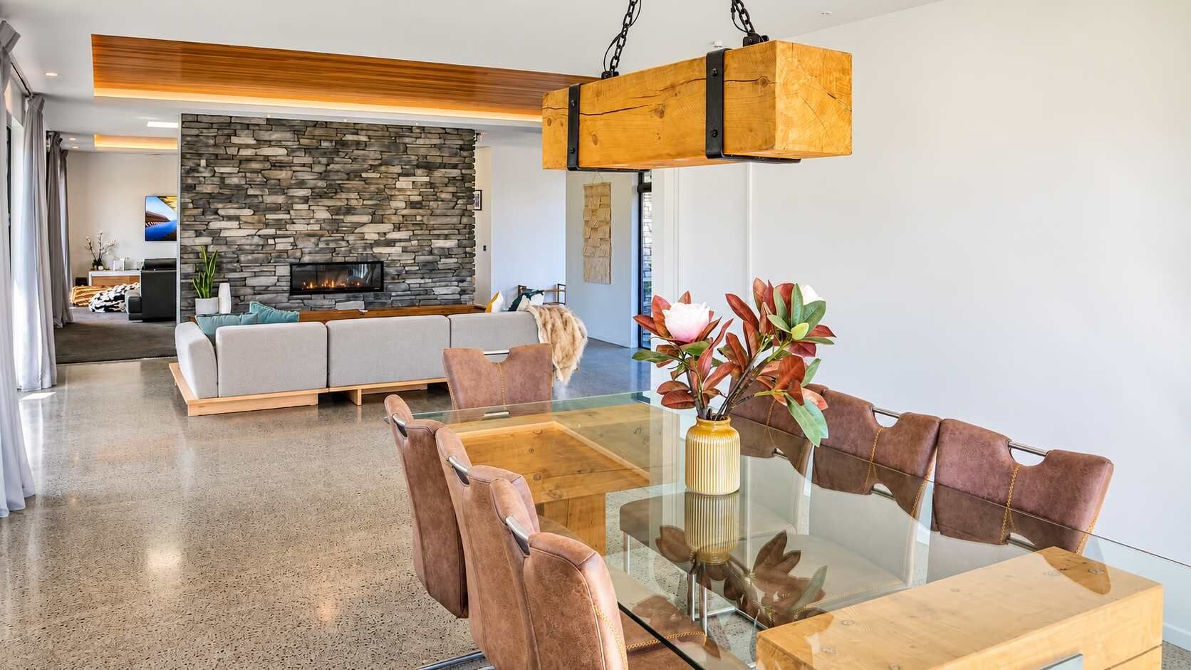 A modern living room with a stone fireplace, a glass dining table, and leather chairs.