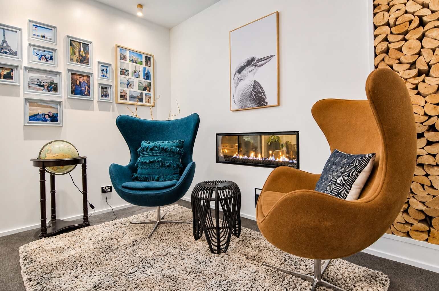 A modern living room with a blue armchair, a brown armchair, a globe on a stand, and a fireplace.