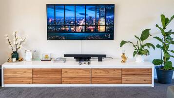 A modern living room with a flat-screen TV mounted on the wall, a wooden and white console table, and two potted plants.
