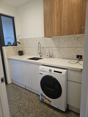 Una cucina compatta con lavatrice integrata, lavello e mobili in legno.
