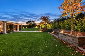 A modern house with a well-maintained lawn, a wooden deck, and a large tree with autumn leaves.