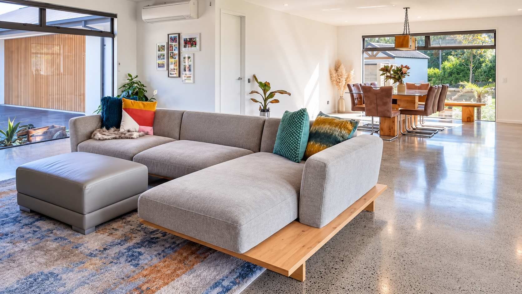 A modern living room with a sectional sofa, ottoman, and a dining area with a table and chairs.