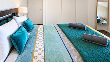 Una habitación de hotel con cama, almohadas, mesita de noche con lámpara y un espejo.