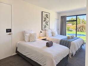 A hotel room with two beds, a framed artwork on the wall, a view of the outdoors through a large window, and a door with a privacy sign.