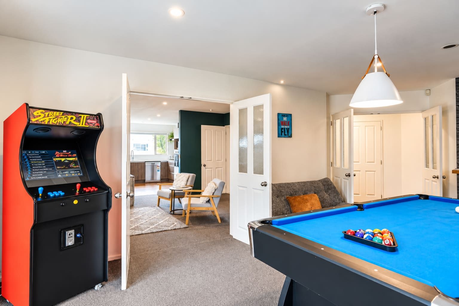 A room with a pool table, a pool, a game console, and a seating area with a view to the outside.