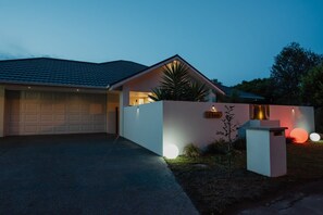 A modern house with a garage, a well-lit entrance, and a small garden area. - Hidden Gem of Christchurch - Sleeps 12 (Christchurch)