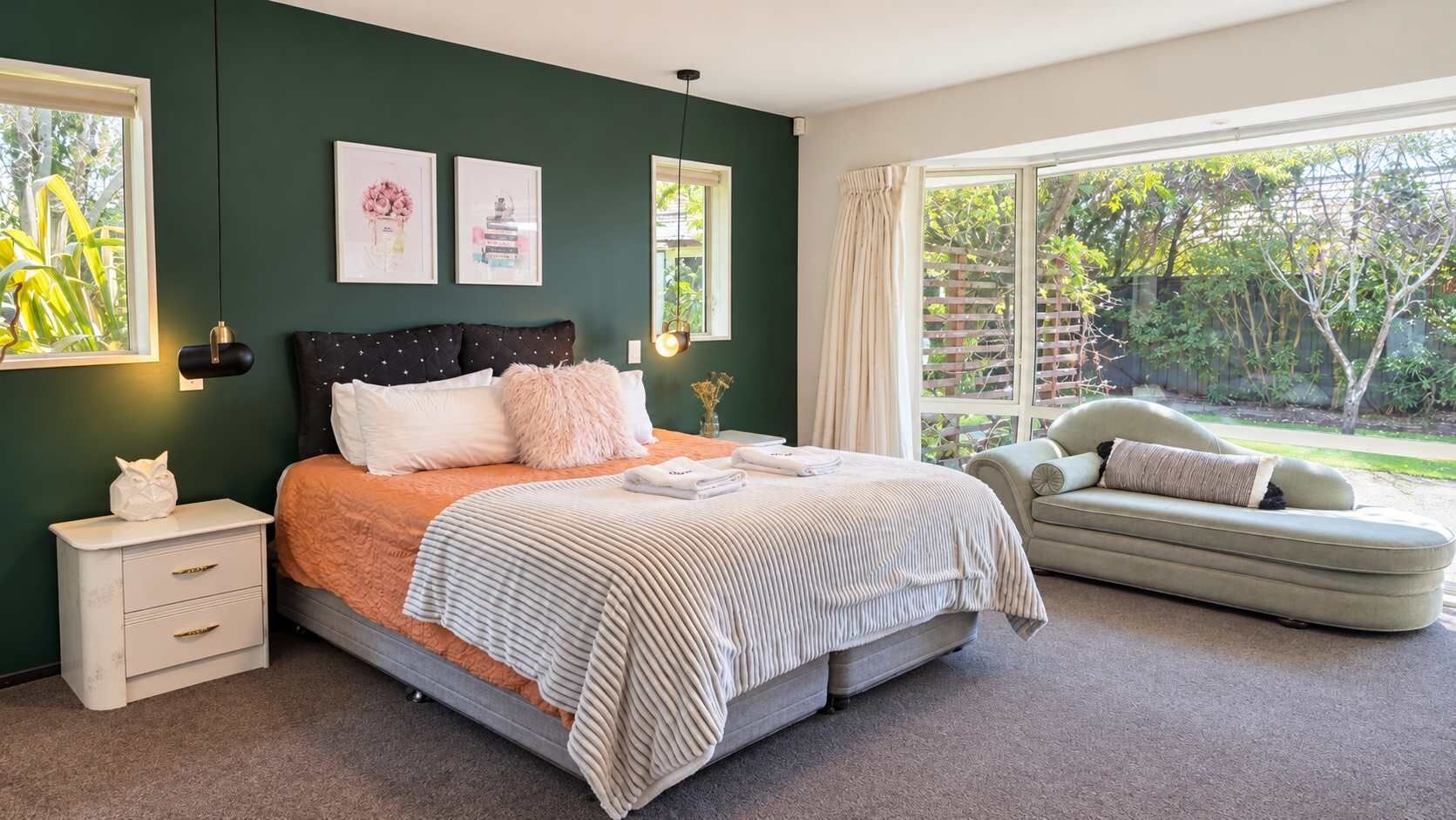 A bedroom with a bed, bedside table, and a window with a view of greenery.