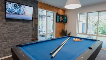 Una mesa de billar con dardos y un televisor montado en una pared de piedra.