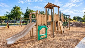 Ein Spielplatz mit Rutsche, Klettergerüsten und einem hölzernen Spielhäuschen.