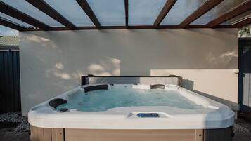 Un jacuzzi bajo una pérgola con estructura de madera y una pared blanca al fondo.