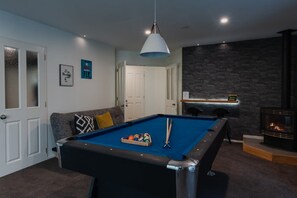 A pool table with cue sticks, a sofa with cushions, a hanging light fixture, and a fireplace. - Hidden Gem of Christchurch - Sleeps 12 (Christchurch)