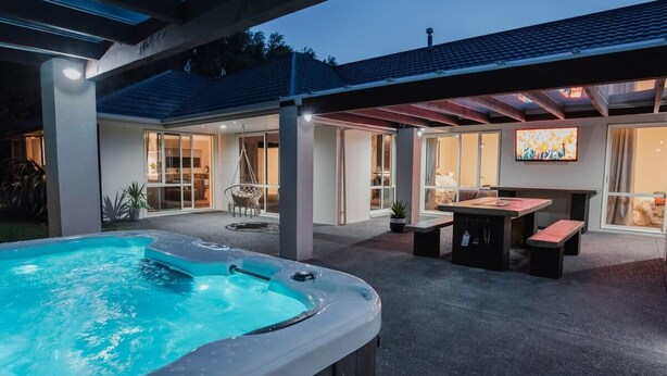 A hot tub in a covered outdoor area with a patio, seating, and a TV screen.