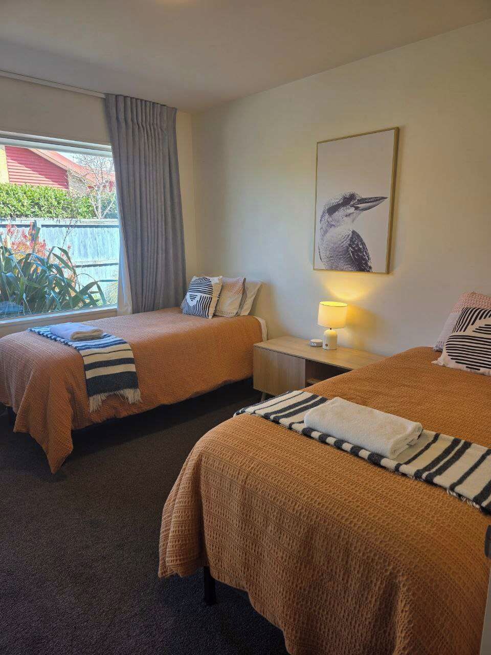 A hotel room with two beds, a nightstand with a lamp, a framed picture on the wall, and a window with curtains.