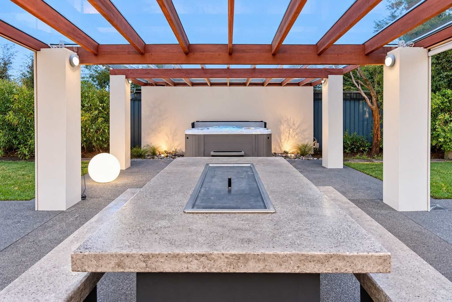 En moderne udendørs terrasse med jacuzzi, stenspidset bord og pergola.