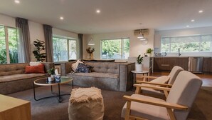 A modern living room with a sofa, ottoman, and chairs, a small coffee table, and a kitchen area with cabinets and a sink.
