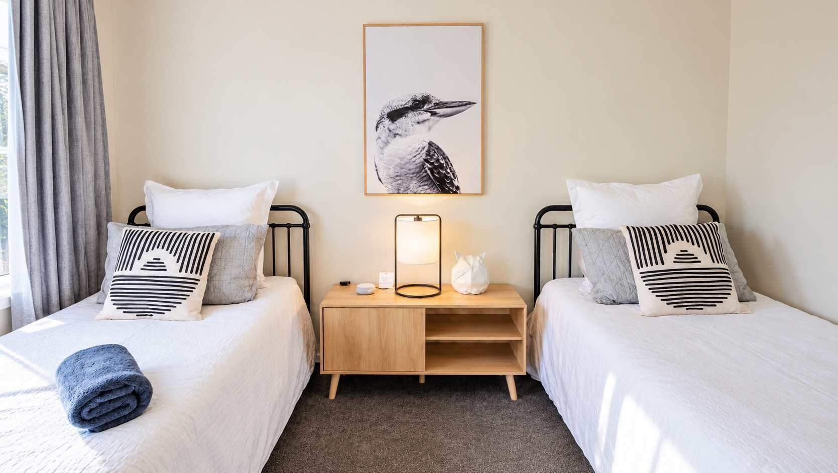 A hotel room with two beds, a nightstand with a lamp, and a framed picture on the wall.