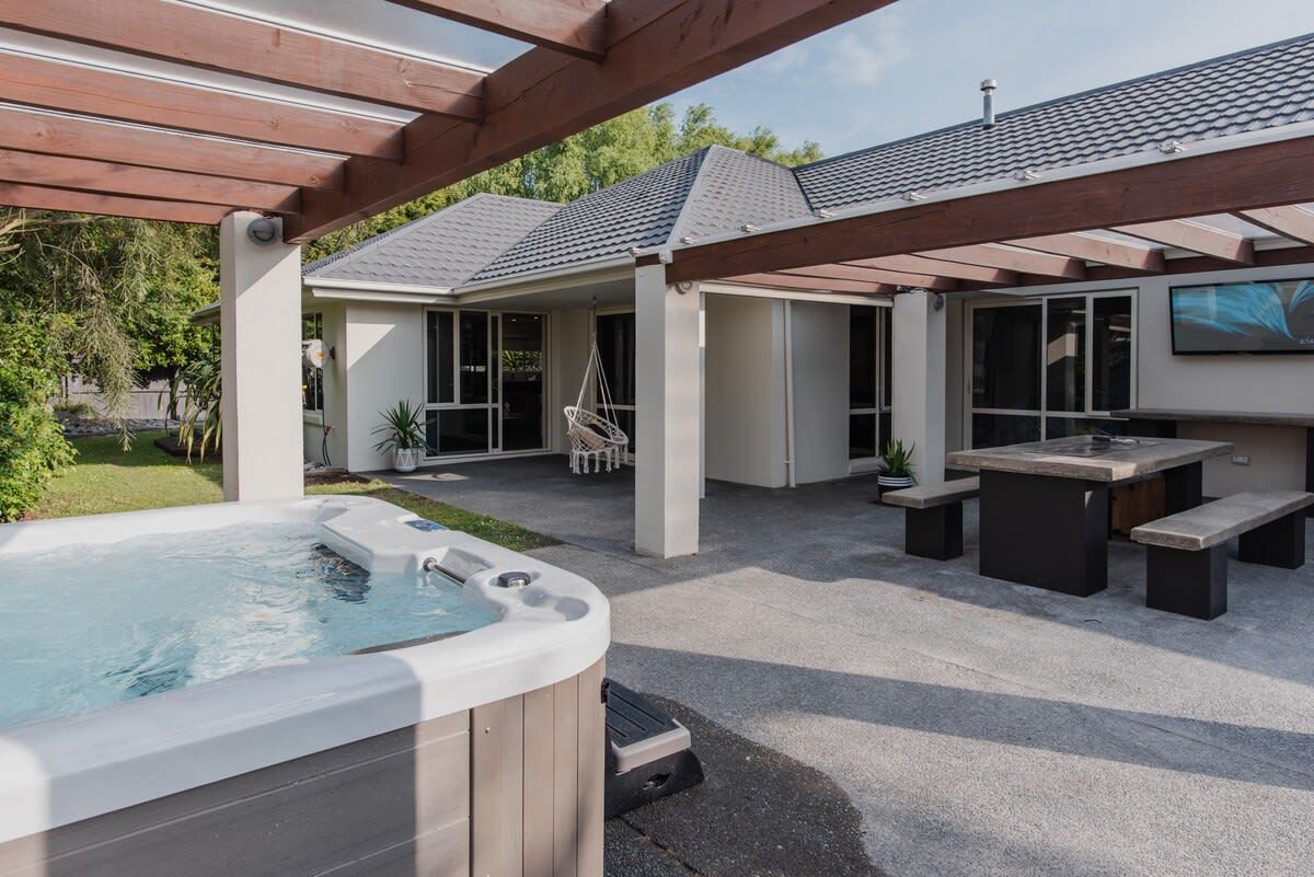 Un patio trasero con jacuzzi, mobiliario exterior y una pérgola.