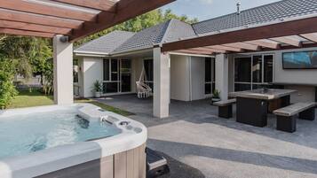 Un patio trasero con jacuzzi, mobiliario exterior y una pérgola.